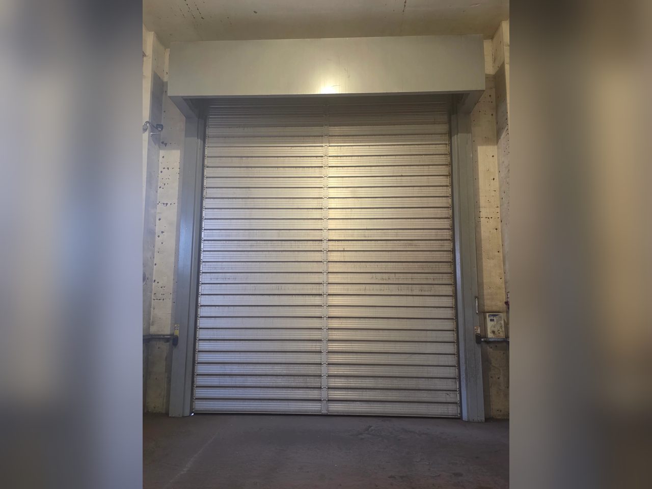 气膜大棚出入口银灰色铝合金硬质涡轮快速门，门体关闭、两侧混凝土门柱实拍